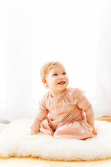 Fototapeta premium Light soft portrait of cute toddler 1 year old baby girl, wearing pink dress, sitting next to window