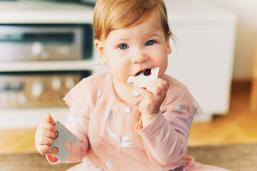 Funny toddler 1 year old girl holding puzzle pieces, chewing one part