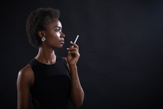 African american woman smoking cigarette at black background.