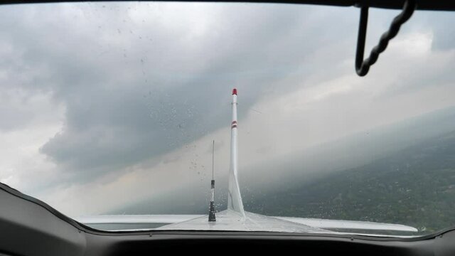 Back window of a small propeller plane, tail in the cloudy, rainy sky