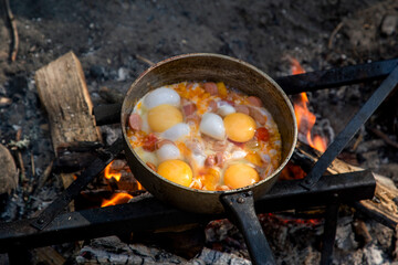 Cooking scrambled eggs over an open fire. Breakfast in nature. Tourist food.