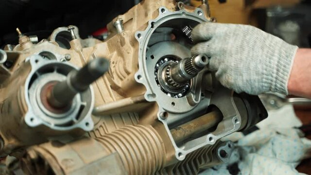 A man locksmith installs a chain and a clutch disc in an ATV engine