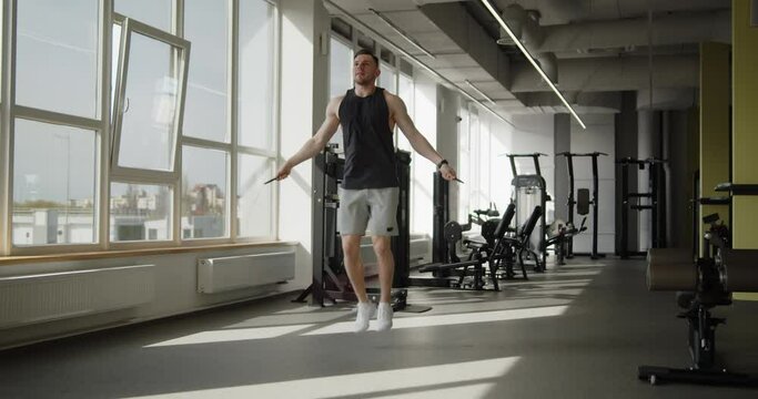 Young attractive muscular athlete works out in a modern gym. Strong man doing jump rope exercises preparing for training. Active healthy lifestyle and wellbeing.