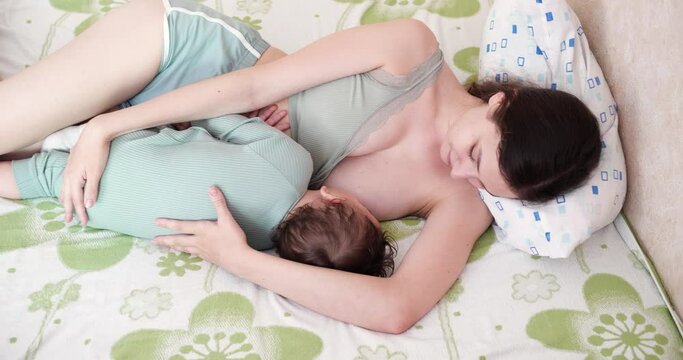 happy mom smiles with happiness breastfeeds her little son in the bed