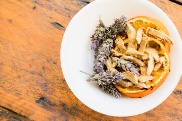 Lavander, orange and ginger for infusions in a white bowl on a wooden table