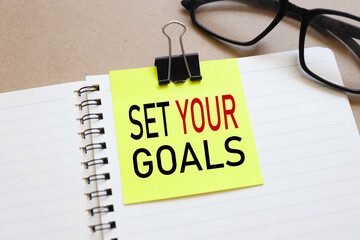 set your goals. sticker attached to a notebook on aa wood background near beautiful glasses