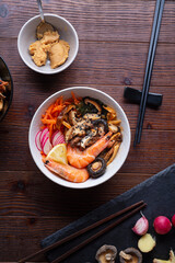 miso soup with mussels, shrimps , shiitake mushrooms and vegatables. served at dark brown wooden table. flat lay