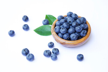 Fresh organic blueberries in bowl on white background. Juicy berries and green blueberry leaves around. Summer healthy super food. Healthy eating concept and lifestyle. 