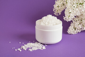 Obraz na płótnie Canvas white sea salt in plastic jar and white lilac flowers on lilac background