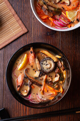 miso soup with mussels, shrimps , shiitake mushrooms and vegatables. served at dark brown wooden table. flat lay