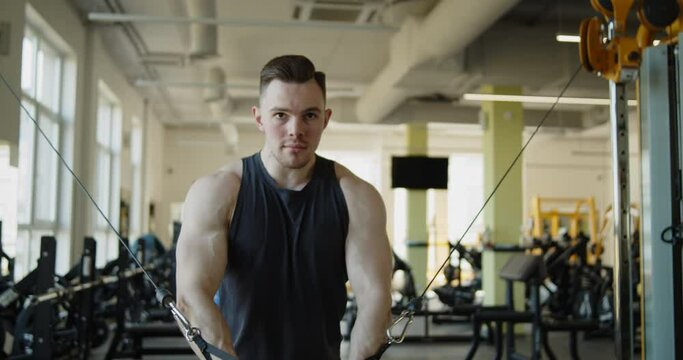 Young attractive muscular athlete works out in a modern gym. Strong fit man doing standing cable crossover exercises during training. Active healthy lifestyle and wellbeing.