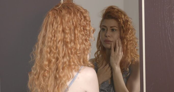 insecurity, doubts - woman checks in the mirror the signs of aging on her face