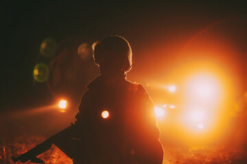 Re-enactor Dressed As Soldier Of USA Infantry Of World War II Holds Submachine Weapon In Hands. Portrait In Low Key. Light From Vehicles Cars Lamps.