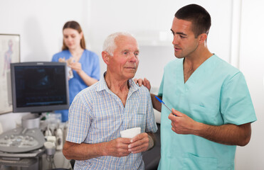 Man doctor and elderly man patient before ultrasound diagnostic, woman on background