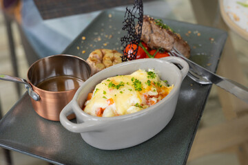 Selective focus and close up shot of well prepared beef juicy steak with luxury decoration of mash potato, sauce and tomatoes served on table for deluxe meal which is cooked by restaurant chef.