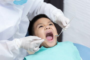 Dentist examining Asian little boy teeth in clinic. Calm and happy