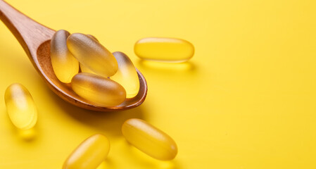 Close up Omega 3 capsules in wooden spoon on yellow background. Fish oil softgels. Horizontal...