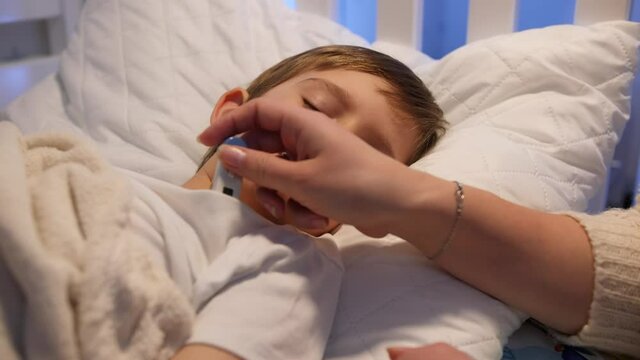 Mother looking at thermometer and checking body temperature of her sick little boy. Concept of children illness, disease and parent care