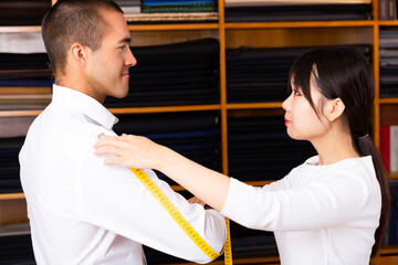 Woman tailor makes measurements of customer clothes in shop
