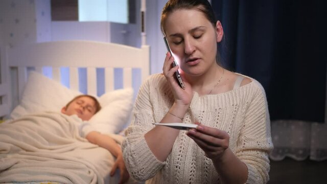 Young woman sitting next to bed of her sick son feeling unwell and talking to doctor. Concept of children illness, disease and parent care
