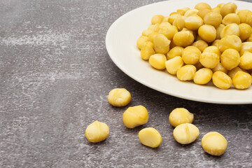 Raw macadamia seeds on plate on stone background