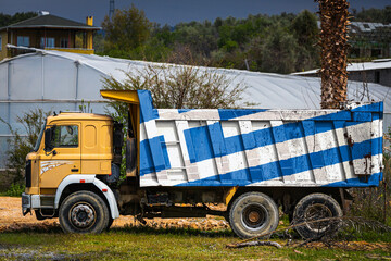 Dump truck with the image of the national flag of Greece is parked against the background of the countryside. The concept of export-import, transportation, national delivery of goods