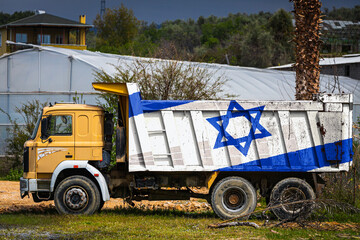 Obraz premium Dump truck with the image of the national flag of Israel is parked against the background of the countryside. The concept of export-import, transportation, national delivery of goods
