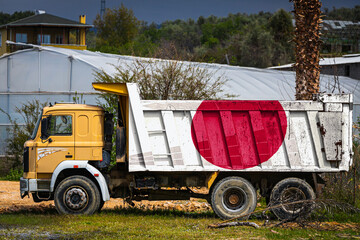 Dump truck with the image of the national flag of Japan is parked against the background of the countryside. The concept of export-import, transportation, national delivery of goods