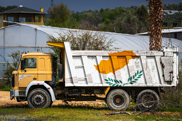 Dump truck with the image of the national flag of Cyprus is parked against the background of the countryside. The concept of export-import, transportation, national delivery of goods