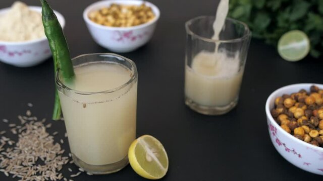 Summer refreshing drink Sattu being decorated with a sliced chili in a glass. Closeup shot of Satu drink pouring in a glass  Sattu Atta  Chana  Dhania  and a slice of lemon together against a black...