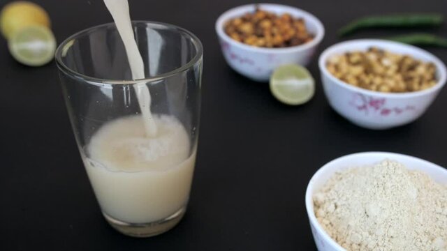 Healthy and cool summer drink Sattu mixed with water pouring in a clear glass. Black Chana  white Chana  a bowl of Satu Atta  green chilies  and sliced lemons kept together - cooking ingredients