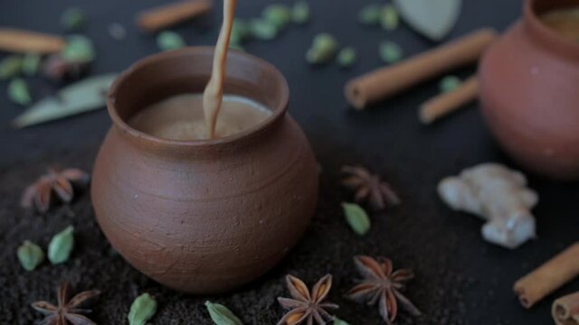 Tasty homemade boiling hot tea poured in traditional clay cups - Indian culture. Famous spices Elaichi  Tej Patta  Dalchini  and cloves kept together against a blurred background - tea-making ingre...