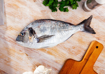 Raw whole dorado fish with garlic and greens on wooden desk