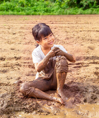 portrait of a little adorable Asian girl sitting smiling and playing in the mud with fun. Family,...