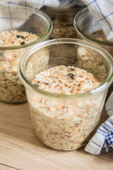 Brotteig von Vollkorn Brot mit Kürbiskernen, Haferflocken, Sonnenblumenkernen, Chia und Leinsaat roh im Glas für Einkochen, Vorrat und Speisekammer auf Tuch und Holz Hintergrund hell