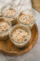 Brotteig von Vollkorn Brot mit Kürbiskernen, Haferflocken, Sonnenblumenkernen, Chia und Leinsaat roh im Glas für Einkochen und Vorrat auf Leinentuch, Holzbrett und Marmor Hintergrund hell