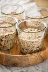 Brotteig von Vollkorn Brot mit Kürbiskernen, Haferflocken, Sonnenblumenkernen, Chia und Leinsaat roh im Glas für Einkochen und Vorrat auf Leinentuch, Holzbrett und Marmor Hintergrund hell