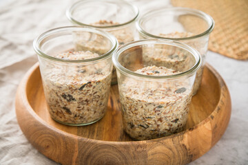 Brotteig von Vollkorn Brot mit Kürbiskernen, Haferflocken, Sonnenblumenkernen, Chia und Leinsaat roh im Glas für Einkochen und Vorrat auf Leinentuch, Holzbrett und Marmor Hintergrund hell