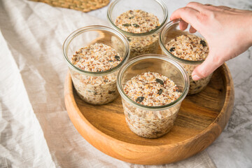 Brotteig von Vollkorn Brot mit Kürbiskernen, Haferflocken, Sonnenblumenkernen, Chia und Leinsaat roh im Glas für Einkochen und Vorrat auf Leinentuch, Holzbrett und Marmor Hintergrund hell