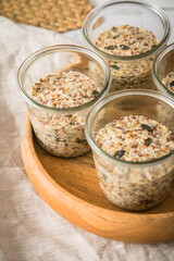 Brotteig von Vollkorn Brot mit Kürbiskernen, Haferflocken, Sonnenblumenkernen, Chia und Leinsaat roh im Glas für Einkochen und Vorrat auf Leinentuch, Holzbrett und Marmor Hintergrund hell