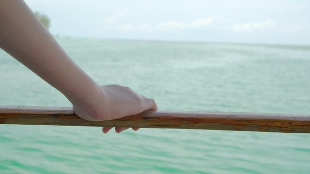 Close up shot of young woman's hand holding wooden railing, standing looking at the outdoor natural landscape of the green sea as the raft moves forward to the sea. in the summer holidays.