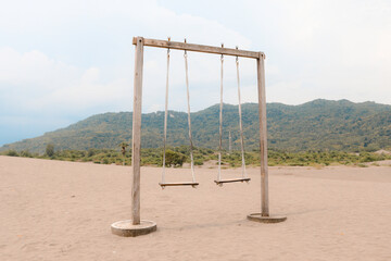 The old rope wooden swing on the desert or sandy beach with mountain background