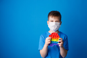 Boy in a mask holds a modern popit toy in his hands .