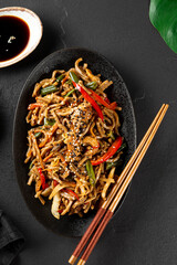 Plate of asian buckwheat soba noodles with vegetables, mushrooms and chicken on dark background close up vertical photo