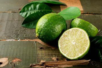 Ripe lime whole and cut in half with leaves on the wooden table close-up