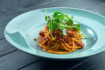 Traditional pasta spaghetti with minced meat and tomato bolognese sauce with arugula, served in a blue plate on a black, wooden background. Italian cuisine