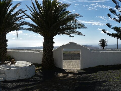 Weisse Steinmauer und Eingangsportal zur Ermita de las Nieves / Kirche mit Palmen im leichten Gegenlicht in Los Valles / Insel Lanzarote