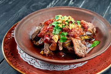 Baked beef with eggplant, nuts, tomatoes and cilantro in clay, served in a bowl on a black background. Restaurant food.