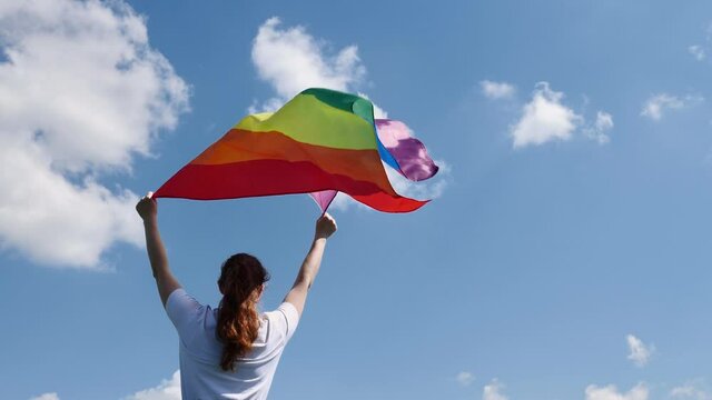 Bisecsual, woman, girl holding a LGBT gender identity flag on a background of blue cloudy sky on a sunny windy summer day during the celebration of the pride month of dignity at the parade