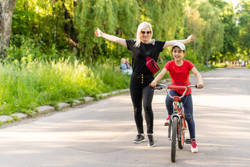 Fototapeta premium Front view portrait of caucasian mother looking through her glasses while helping her daughter to ride the bike